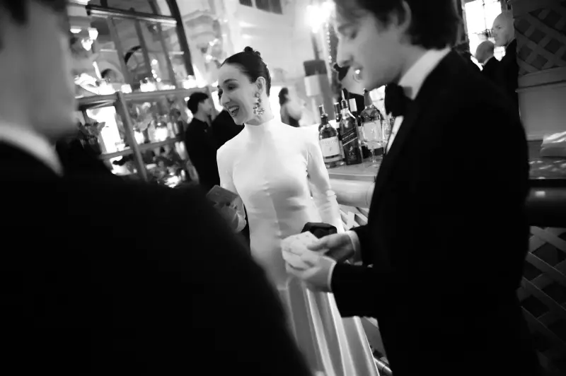 Black and white photo of Jacob in a tuxedo performing card magic for a smiling guest at a bar