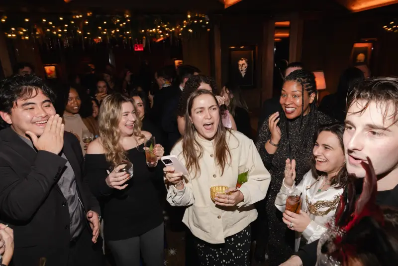 A crowd of guests gasping and laughing after a card trick at a holiday party