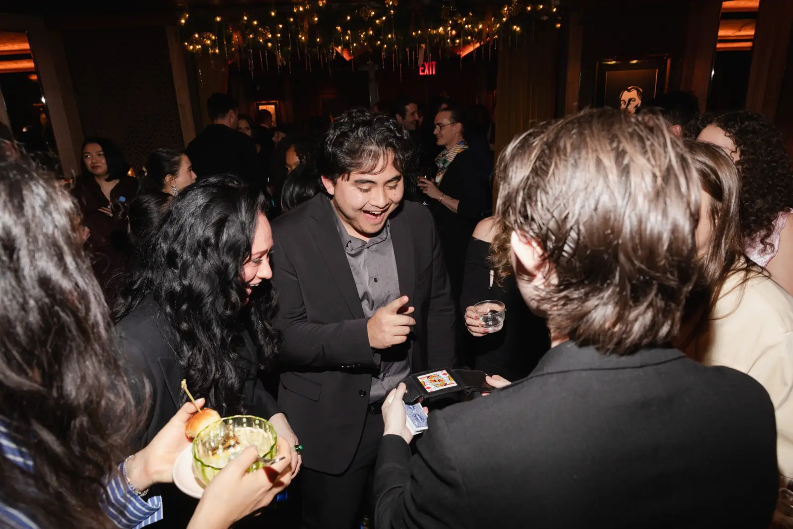 Jacob performing a card trick for a laughing guest at a cocktail party